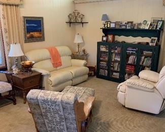 a corner of the family room; white leather recliner; recliner love seat; wagon wheel oak chair and ottoman; lamps; 4 door book case; books; brass lamps