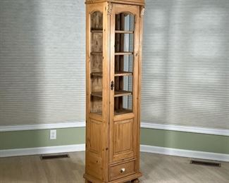 LIGHT PINE NARROW DISPLAY CABINET  |  Glazed glass door and sides, carved terminals, with a single lower drawer - l. 19 x w. 14 x h. 71 in.