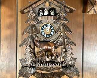 FOREST SCENE CUCKOO CLOCK  |  Cuckoo clock with Swiss musical movement, Gueissaz - Jaccard label on verso, having a headboard featuring dancing people above a forest scene with deer; leaf shaped pendulum and three pine cone weights - w. 12 x h. 52 in. (approx)
