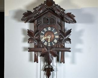 CARVED OAK CUCKOO CLOCK  |  Crested by a carved deer with leaves over an open clock face with Roman numerals, carved leaves wooden pendulum, and three brass pinecone weights - h. 24 in. (with pendulum)
