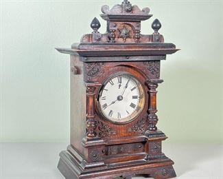 MUSICAL OAK SHELF CLOCK  |  Having a carved decorated oak case, steel and brass movement engraved with an "F" connected to a musical cylinder - l. 7 x w. 5 x h. 11.5 in.