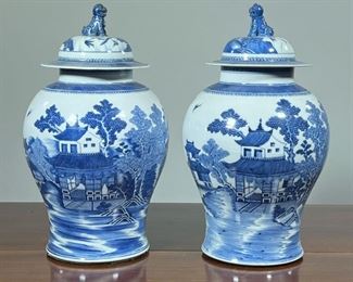 (2pc) PAIR BLUE & WHITE GINGER JARS  |  Chinese lidded jars crested by foo dog finials, each showing a village scene in countryside next to a flowering tree - h. 16 x dia. 9 in.
