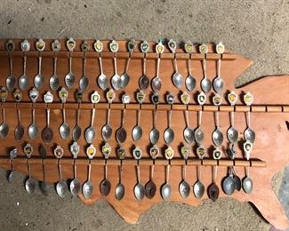 Souvenir spoon collection on wooden cutout of the USA.  The bowls of the spoons are rough.