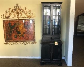 Tall narrow black cabinet and wood wall panel with metal crown