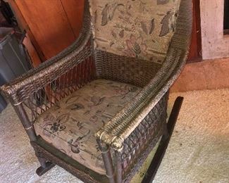 Side View Forward Direct Close Up Of Wicker Antique Rocker With Original Upholstery From The Family Boathouse Circa 1929-1931. THE BEMIS RIDDELL FIBRE CO. IN SHEBOYGAN, WIS., WAS COMMISSIONED IN 1929-1931 TO MANUFACTURE THE FAMILY WICKER COLLECTION OF FURNITURE - RARE ORIGINAL UPOLSTERY IN TAPESTRY DESIGNS