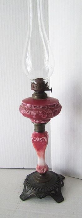 Lot 6   C/1880 Ladies petite Vanity Oil Lamp, Victorian scroll decoration with red overlay on white glass with fancy iron base, 19" h. x 6" dia.  Condition:  Minor wear overall from use, no other damage found.  