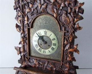 Lot 17   C/1880 German Black Forest carved Mantle Clock, 8 day time and strike, circular brass French movement stamped "Marti", engraved bronze faceplate w/overlaid white brass chapter ring.  27 1/2" h. x 17" w. x 8 1/2" deep.  Condition:  Minor wear overall, 1 leaf tip re-glued, movement not evaluated but key and pendulum are present. 