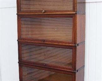 Lot 34   C/1910 "Macey" Stacking Oak Bookcase, 6 sections plus top and bottom (8 pcs. total), 88" h. x 12 1/2" d. x 34" w.  Condition:  2 Brass knobs replaced, some wear and fine scratches from use, wavy glass in all panels, 1 section has a small veneer loss in right hand inside corner.  Some back panels are wavy at the edges.  