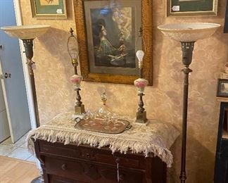 Beautiful old East Lake cabinet missing its marble top. Lovely old fringed spread from Italy, matching hand painted lamps - I think the flower is a chrysanthemum, a pair of Torchiere floor lamps, antique religious art & a pair of pretty floral antique prints
