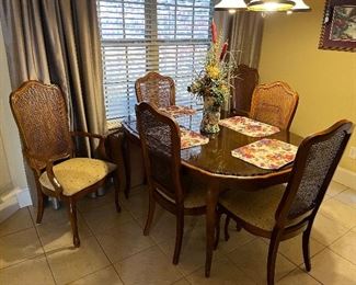 Dining table with 6 cane back chairs and 2 leaves has a glass top for the small size