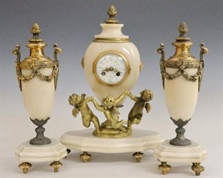 A turn of the century French three-piece clock set by Japy Freres.  8-day time and strike movement with a convex porcelain dial, Arabic numerals and fancy filigree hands.  Urn form Cream Marble case surrounded by Gilded cast Cherubs on a shaped base with cast feet, accompanied by two matching Marble garnitures with Gilded cast Cherub masks and Acanthus Leaf details.  Some surface wear, repair to Cherubs, wear and repair to Gilding, running momentarily when cataloged.  Clock is 16 1/2" high and the garnitures are 14 3/4" high.  ESTIMATE $400-600
