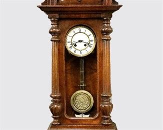 A late 19th century Kienzle German wall clock.  8-day spring driven time and strike movement with a two-part porcelain dial, Roman numerals and embossed Brass pendulum.  Walnut case with shaped crest over an arched door with applied fluted pilasters and shaped drop.  Old finish with some wear, dial wear, replaced crest, strike hammer loose, not running when cataloged.  40" high.  ESTIMATE $200-300

