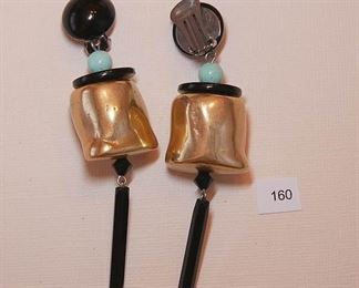 Attributed to Angela Caputi. Clip back gold Tone. Each drop earring measures approx. 3 3/4”.  The top portion is a half round cabochon measuring approx. 17mm in diameter. Attached as the drop is a round light blue bead, a flat black disc on top of a large gold tone chunky hollow, polished form bead about 23 mm in length and holding a black faceted bead and a black hexagon straight rod bead.