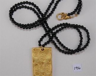 CYN N. Y. C. Gold Tone. The gold Tone Plaque Matches the ones in Item #195 and is attached to a strand of black onyx/glass beads measuring 4mm in diameter each. The strand measures approx. 33” in length and has a hood tone lobster claw clasp.