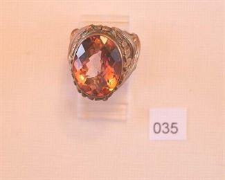 Possibly Sylvia Dahl or Sylvanias Dweck. Gold Tone ladies ring approximately size 7.  The ring has an overall raised floral and banded motif. At the center is one oval faceted, transparent pink stone measuring approximately 15x20mm bezel set.