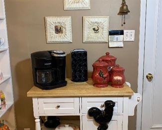 This kitchen unit features 2 drawers and open shelving as well as a cabinet. Sitting on the butcher block top is a large Keurig as well as a Keurig pod holder. Notice more of the rooster collection surrounding it.