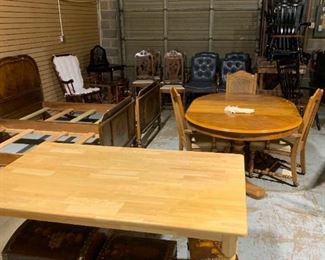 Pine table and underneath 3 nesting trunks Game table behind with leaf and 3 rolling chairs. Further back rocking chair, small writing desk or vanity, piano stool, vintage dining chairs, deep blue leather office chairs (3 arm chairs, 1 executive rolling chair), Black and wood kitchen chairs.