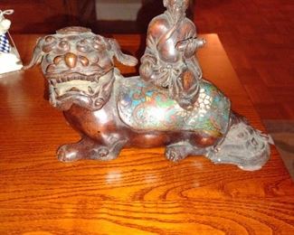 This appears to be Chinese bronze 18th c. Decorated with cloisonné. A scholar holding a scroll, riding a fu dog. I think it is of provincial manufacture.