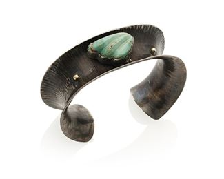 155
Late 20th century
Jolene Eustace (B. 20th Century, Zuni/Cochiti Pueblo)
A silver and 18k gold cuff bracelet
Stamped to interior: JAE / Sterling; further etched: JAE / SS / 18K
A concave textured oxidized sterling silver cuff accented with18k yellow gold balls and with central bezel set carved turquoise stone
6.75 total inner C x 1" H, with a 1.125" gap<br />64.2 grams gross
Estimate: $700 - $900