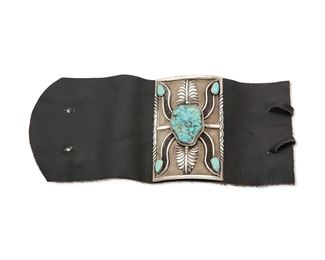 221
Mid-20th century; Dine
A Small Navajo Silver And Turquoise Ketoh Arm Guard
Appears unmarked
A ketoh arm guard with central large turquoise set to sandcast silver with applied foliate motifs and incised edges, mounted on a black leather band
Ketoh: 3.125" H x 2" W<br />74.2 grams gross
Estimate: $400 - $600