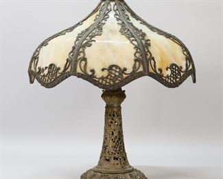 92	B&H Style Slag Glass Lamp	8 panel slag glass lamp in the style of Bradley & Hubbard. Openwork base and caramel slag glass shade with metal overlays and acorn finial. Unsigned. 22"H including finial, shade 17 1/4"-diameter. Sections of metal overlay missing throughout shade; cord cracking and splitting.
