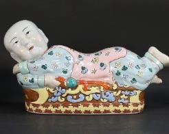 141	Three Chinese Figural Porcelain Pillows	"Three Chinese figural porcelain pillows. 20th century. Chinese marks to undersides of pair of pillows. Paint losses to surface of boy's tunic on largest figure. Dirt and wear throughout all figures. Chipping and roughness to edges of bases on pair of pillows. 

Largest pillow: 8 1/2"" H x 15 1/4"" L x 5"" W"
