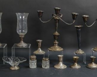 283	Lot of Weighted Sterling and Sterling Glassware	Lot of weighted sterling pieces and sterling accented glassware. Includes a pair of Gorham candelabra, trumpet vase, pair of candlesticks, three single candlesticks, pair of candlesticks with hurricane shades, one crystal dish with sterling base, one crystal dish with silverplated base, one glass condiment jar with sterling lid and coin silver spoon, and one glass jar with sterling lid. Bases of vase, candlesticks, and candelabra are all dented. Vase top also includes dents. Lower rims of hurricane shades have chips, in addition to some chipping on the top rim of one shade. Flea bites to condiment jar. Glass jar has a dented lid with a broken hinge, interior stopper is chipped and frozen. Candelabra measure 12 1/4" in height.
