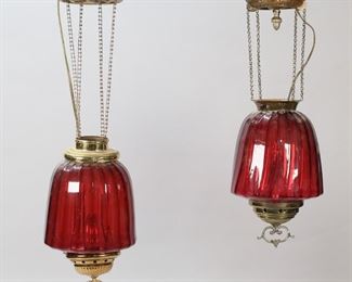 326	Pair of Cranberry Glass Hanging Fixtures	Pair of cranberry glass and brass hanging fixtures. One missing cap, with mismatched ceiling mounts. Fixture with acorn finial 19 1/2"L from ceiling cap, 11 1/2"L from top of fixture. Ceiling cap on fixture with acorn finial bent and dented, loss to patina on bottom finial; fixture with cap large chip to lower rim.
