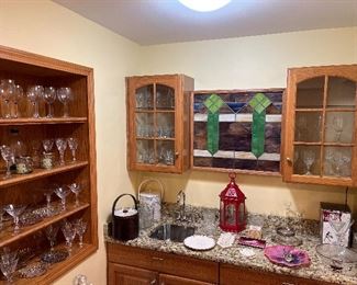 Family Room-Bar Area:  Stemware; ice buckets (one is a tortoise look by Georges Briard; the other has a Dow-Jones theme); and miscellaneous items are all displayed behind the bar.