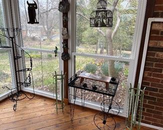 Sun Room:  A small metal plant/tea cart is flanked by plant stands and wall decor.  