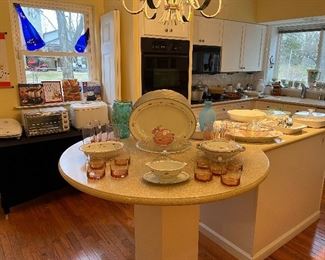 Kitchen:  Four pieces of NORITAKE "Rose Dawn" china  and pink glassware greet you as you enter the kitchen.  In the background are boxed fondue sets; a George Foreman Grill; a tabletop convection oven; a Bread Machine; hand mixer; blender; cookware; bakeware; Pyrex; Corning Ware; and more!