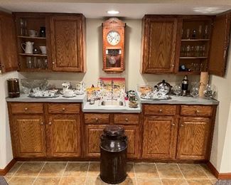 Lower Level:  A wall clock (key is with the cashier) is flanked by cabinets and counters which display a vintage punch bowl set with 16 cups and ladle; DENBY "Langley Troubadour" dishes; and bar ware.  The milk can in the foreground is from the "Beatrice Creamery."