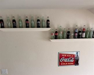 Collection of commemorative and vintage bottles of Coke, and small Coca-Cola metal sign