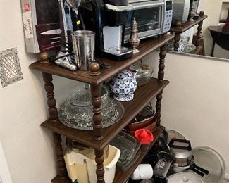 A dark-wood short bookshelf with some of the kitchen appliances and supplies.