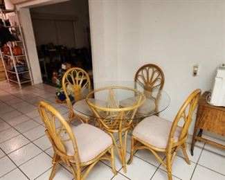 Rattan 5-piece dining set with round, glass top table and four matching chairs with cushions.
