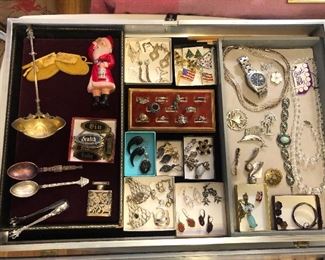 Case items: Sterling ladle, old Seattle souvenir spoons, sterling tongs, celluloid Santa, jewelry including sterling earrings, chains & rings, Swarovski crystal necklace & bracelet, Xmas tree pins & more