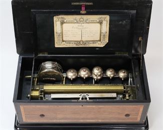 21	Swiss Cylinder 8 Tune Drum & Bell Music Box	8 tune swill cylinder music box with drum and 6 bells. Musique de Geneve sheet inside lid with 8 tunes. Wooden case with inlaid floral decoration on lid. Working condition, cylinder rotates and plays, hammers strike bells and drum. 26 1/4"L x 13 1/4"D x 10 1/8"H, cylinder 15 1/4"L. Losses to inlay on lid; chips, splits and losses to veneer on case, lever for bells does not hold in locked position; no key for case. From the collection of a prominent Connecticut family.
