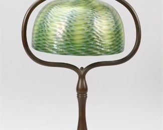25	Tiffany Studios Damascene Harp Lamp.	Tiffany Studios (New York 1878-1933) Bronze desk lamp with a green damascene glass shade. Inside of fitter on shade marked "L.C.T. Favrile". Bronze harp base marked on bottom "Tiffany Studios New York 424" and "1648". Shade 7" in diameter. Shade fitter 2 1/4" in diameter. Base 17 3/4" Tall. Base is missing one screw to hold lamp shade in. Lamp has been tested and is in working order.
