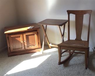 A two-door oak-finish stand, a TV tray that’s part of a four-piece set and an antique oak rocking chair with cane bottom. 