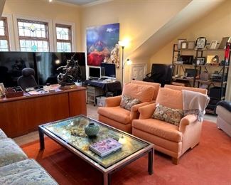 1972 Romeo Rega acid etched MCM coffee table.  Pair of beautiful orange club chairs.  Pair of 75” Sony Bravia TV’s.  Apple computer.  Audio equipment.  This room is packed and it’s great!