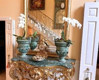 Gilt antique entry table with marble top, bronze ram’s head planters with real orchids, French clock, oversized gilt mirror