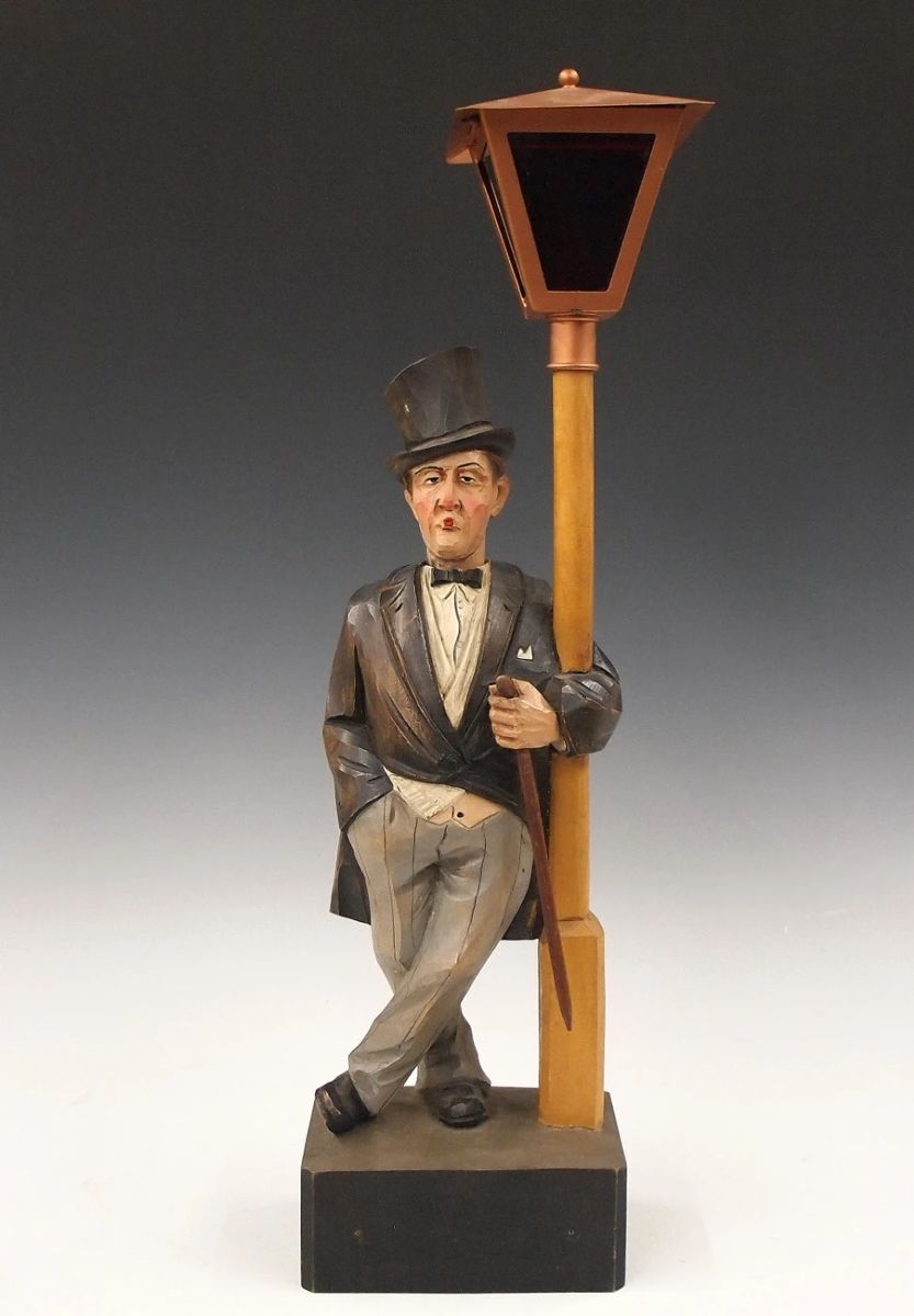 Lot 2: A mid 20th century German clockwork "Whistler" figure by Karl Griesbaum, Triberg.  Carved wooden automaton figure whose head moves and whistles a tune when activated via Brass key wind movement with bellows.  Original painted finish, with a battery operated street lamp.  Stamped "K G" Trademark with songbird.  Minor wear, working when cataloged.  18 3/4" high overall.  ESTIMATE $600-800
