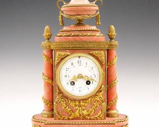 Lot 6: A late 19th century French Louis XVI Style mantel clock by A. D. Mougin, Paris.  8-day time and strike movement with convex porcelain dial, Arabic numerals, hand painted floral swags and fancy Gilded filigree hands.  Pink Marble case with Gilded Bronze mounts, features a shaped top with urn finial over a facade with foliate swags flanked by turned columns with floral appliques on an oval  base with beaded Bronze feet.  Some wear, minor damage to Marble, running when cataloged.  13" high overall.  ESTIMATE $600-800
