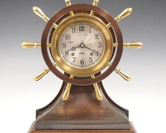Lot 8: A mid 20th century Chelsea Clock Co. "Mariner" model ship's clock.  8 day time and strike movement with Silvered dial, Arabic numerals and Ships Bell striking, marked "Donovan & Seamans Co., Los Angeles" serial #673267.  Bronze "Yacht Wheel" case with a Bronze and Mahogany base.  Some surface wear, tarnish, running when cataloged.  13 1/2" high overall.  ESTIMATE $600-800
