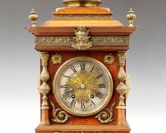 Lot 14: A late 19th century Lenzkirch Bracket clock.  8-day spring driven time and strike movement with engraved Brass dial center, Silvered chapter ring and Roman numerals, serial #568480 indicates a production date of 1881.  Walnut case with cast Brass Dome, finials and appliques, molded circular Brass dial door flanked by Brass columns and Bacchus mask side medallions, on a molded base with Brass mask feet.  Older finish with minor wear, running when cataloged.  20 1/4" high overall.  ESTIMATE $800-1,200
