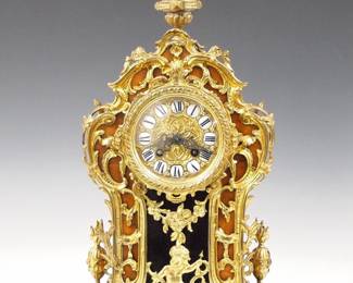 Lot 19: A late 19th century Lenzkirch Louis XV Style table clock.  8-day spring driven time and strike movement with embossed Brass dial and Roman numerals on porcelain markers, filigree hands and a fancy cast Brass bezel, serial #764131 indicates a production date of 1886.  Louis XV Style Burl Walnut case with extensive cast Brass appliques which continue onto the sides of the shaped case, includes Cupid below a wreath surrounded by foliate swags.  Original finish with slight wear, tiny flake on 8:00 marker, running when cataloged.  18 3/4" high overall.  ESTIMATE $800-1,200
