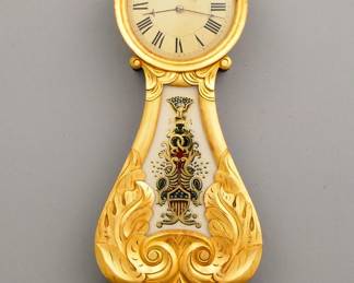 Lot 20: A 19th century American Lyre front Banjo clock.  8-day weight driven time only movement with a painted Iron dial and Roman numerals.  Mahogany case with Gilded decoration, turned top finial over a circular dial door with convex glass and foliate carved lower panel with reverse painted glass, shaped drop with beaded detail and turned bottom finial.  Some case wear, dial re-painted, replaced lower glass, running when cataloged.  37 1/2" high overall.  ESTIMATE $1,000-2,000
