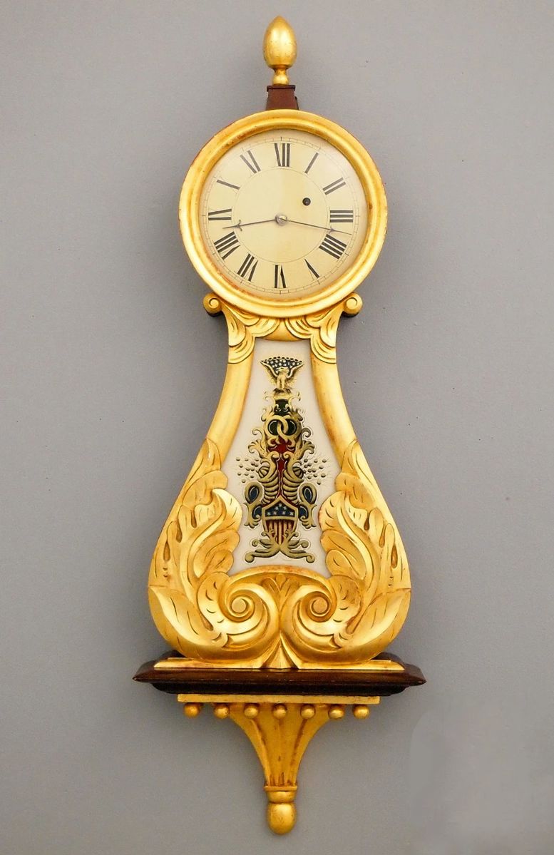 Lot 20: A 19th century American Lyre front Banjo clock.  8-day weight driven time only movement with a painted Iron dial and Roman numerals.  Mahogany case with Gilded decoration, turned top finial over a circular dial door with convex glass and foliate carved lower panel with reverse painted glass, shaped drop with beaded detail and turned bottom finial.  Some case wear, dial re-painted, replaced lower glass, running when cataloged.  37 1/2" high overall.  ESTIMATE $1,000-2,000
