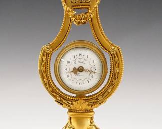 Lot 21: A turn of the century French Gilded Bronze Lyre clock by "F Deux, Paris".  8-day time only movement with platform escapement, convex porcelain dial with Arabic numerals, Gilded filigree hands and hand painted floral swags marked " G. Fabre, Paris".  Gilded Bronze Lyre form case surmounted by a mask of the Sun God Apollo with floral swags on an oval foliate pedestal with beaded feet.  Minor wear, running when cataloged.  13" high overall.  ESTIMATE $800-1,200
