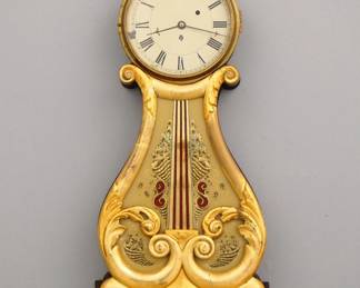 Lot 25: A 19th century Boston area Lyre front Banjo clock.  8-day weight driven time only Brass movement with painted metal dial.  Mahogany case with original Gilded finish, Brass bezel upper door, carved lyre central panel with reverse painted glass over a single lower door with reverse painted glass panel.  Some wear and older repairs, replaced Eagle finial, running when cataloged.  31" high overall.  ESTIMATE $1,000-1,500
